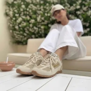 Tenis Miu Miu beige en gamuza y tela con cordones gruesos, logo lateral dorado y suela de caucho, lucidos en un entorno urbano con estilo casual.
